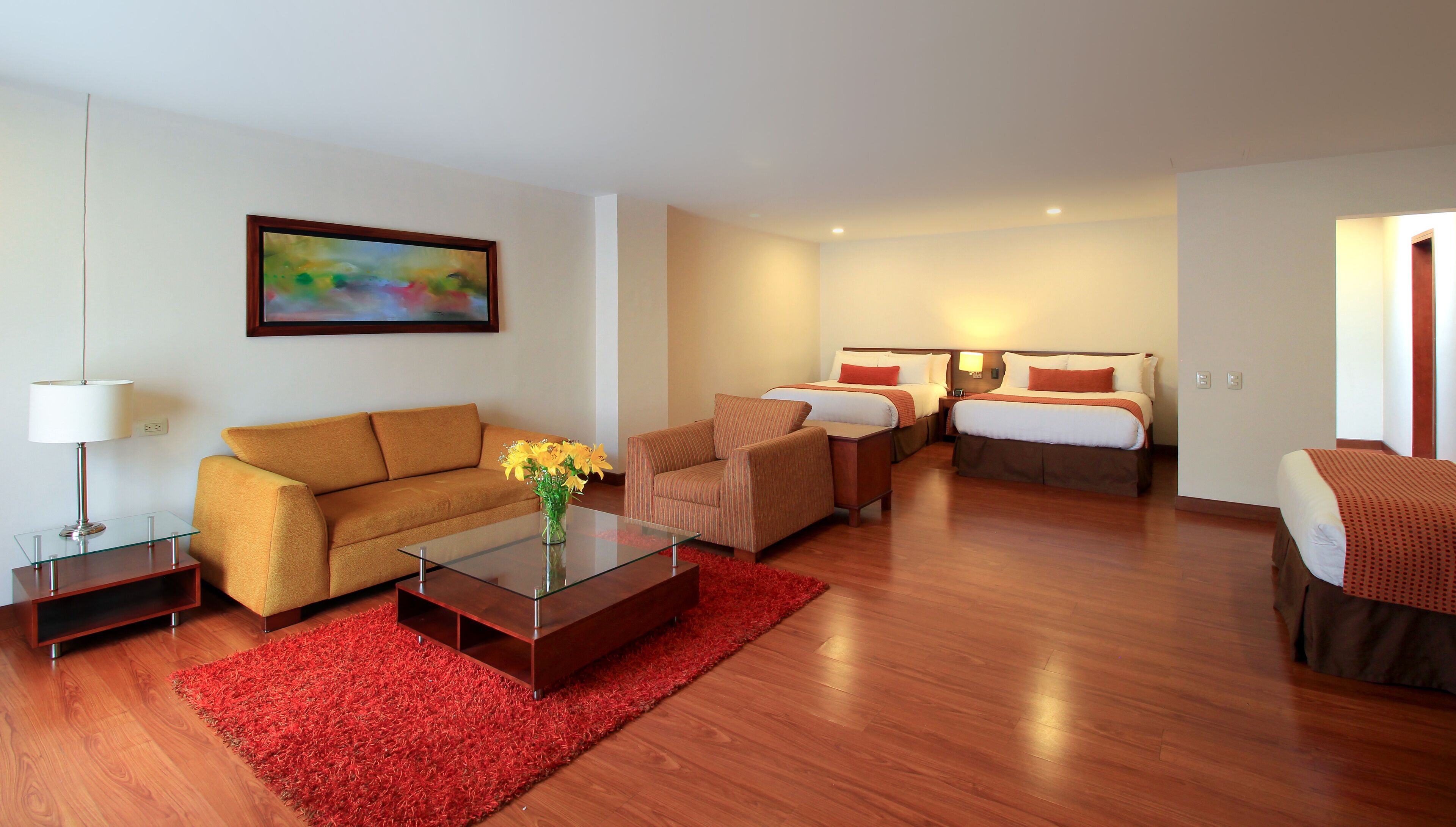 A hotel room with a sofa, a chair, a bed, a nightstand, a lamp, and a painting on the wall.
