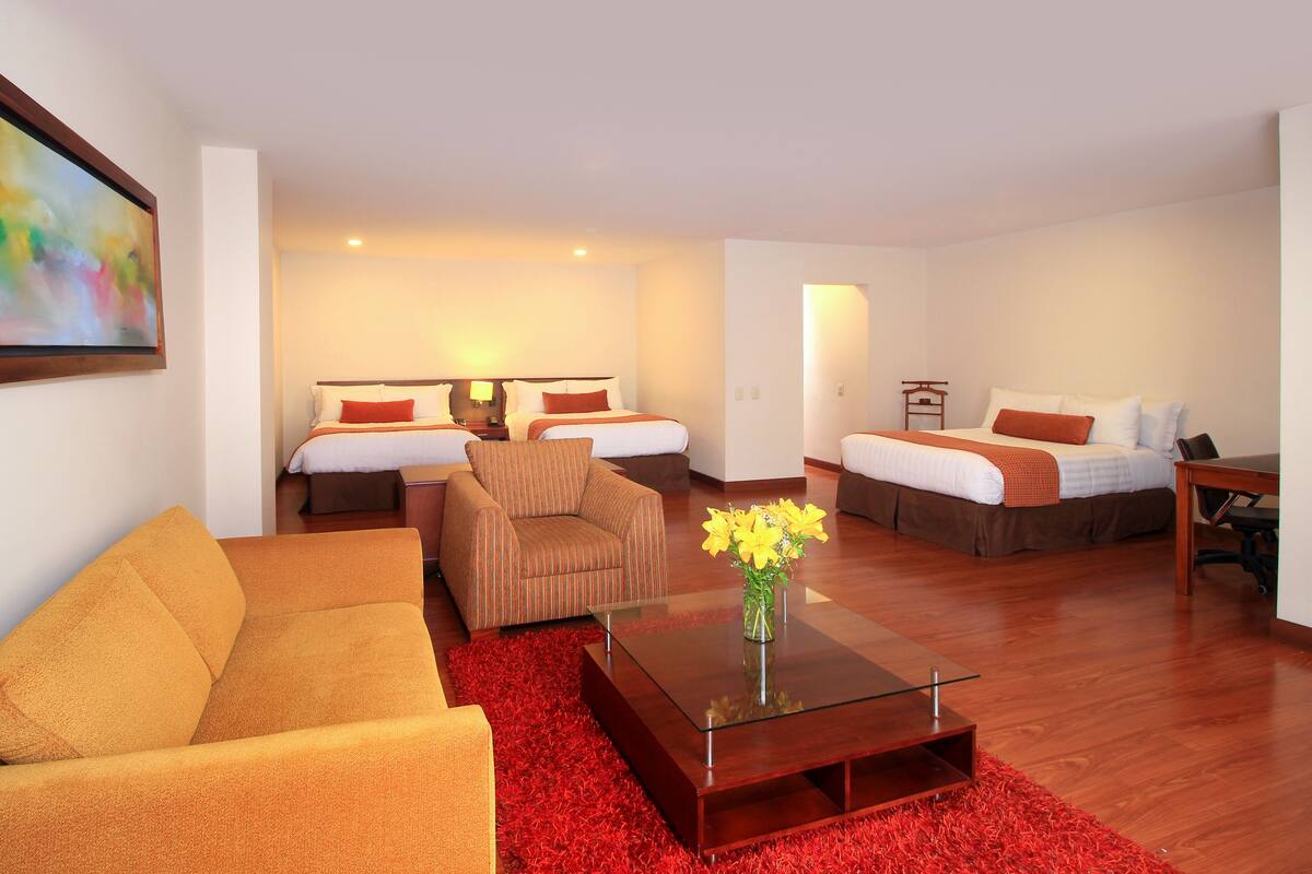 A hotel room with a sofa, two single beds, a small table, and a red rug.