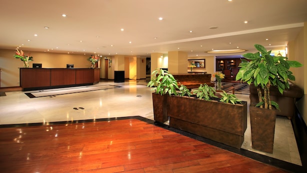 A hotel lobby with a reception desk, seating area, and potted plants. - Hotel Windsor House Inn By GEH Suites (Bogotá)