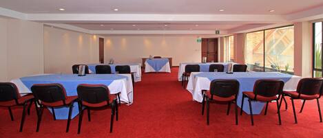 A conference room with tables and chairs, large windows, and a red carpet.