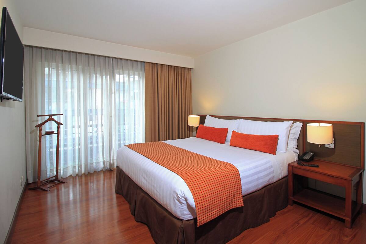 A hotel room with a large bed, two bedside lamps, a wooden nightstand, and a TV mounted on the wall.