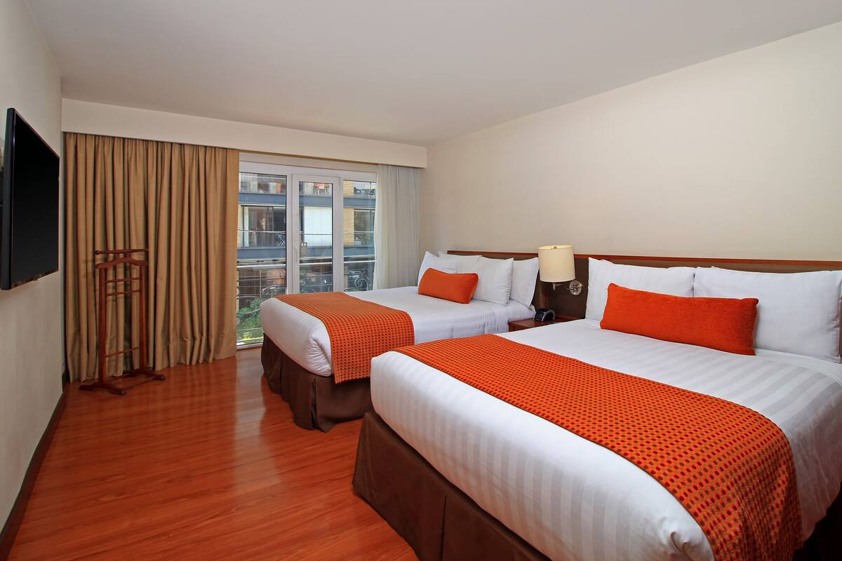 A hotel room with two beds, a TV, a window with curtains, and a wooden floor.