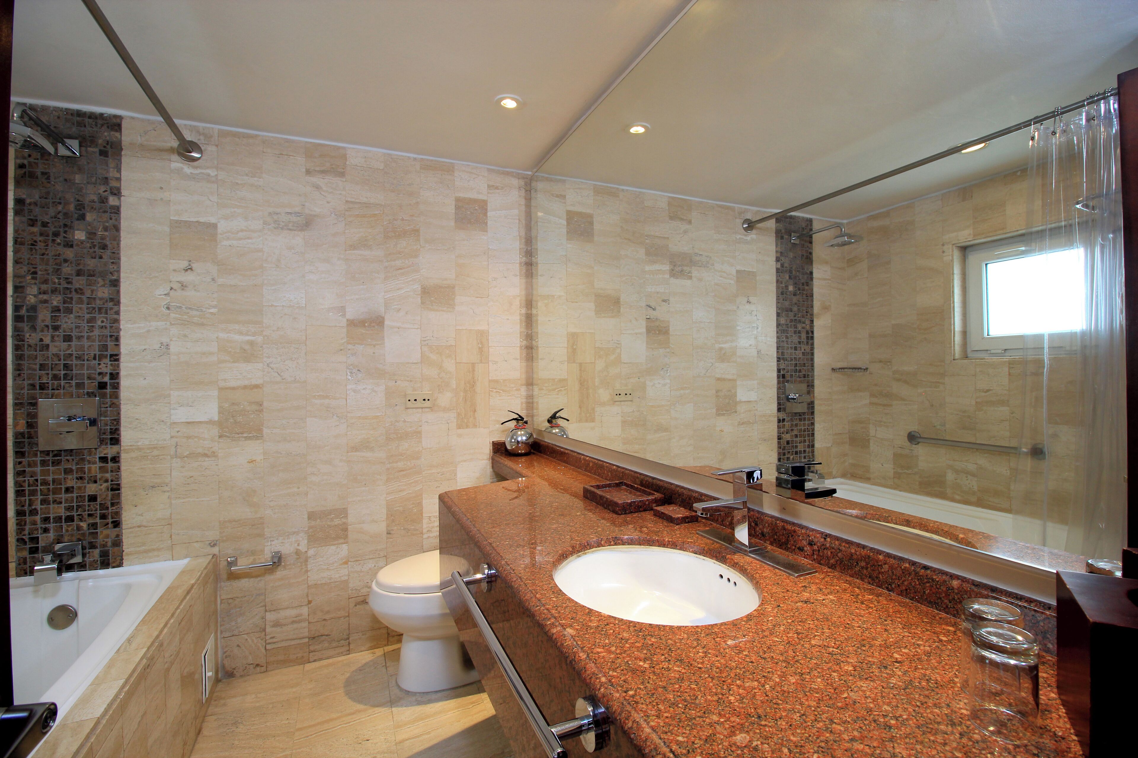 A modern bathroom with a granite countertop, a white sink, a large mirror, and a shower area.