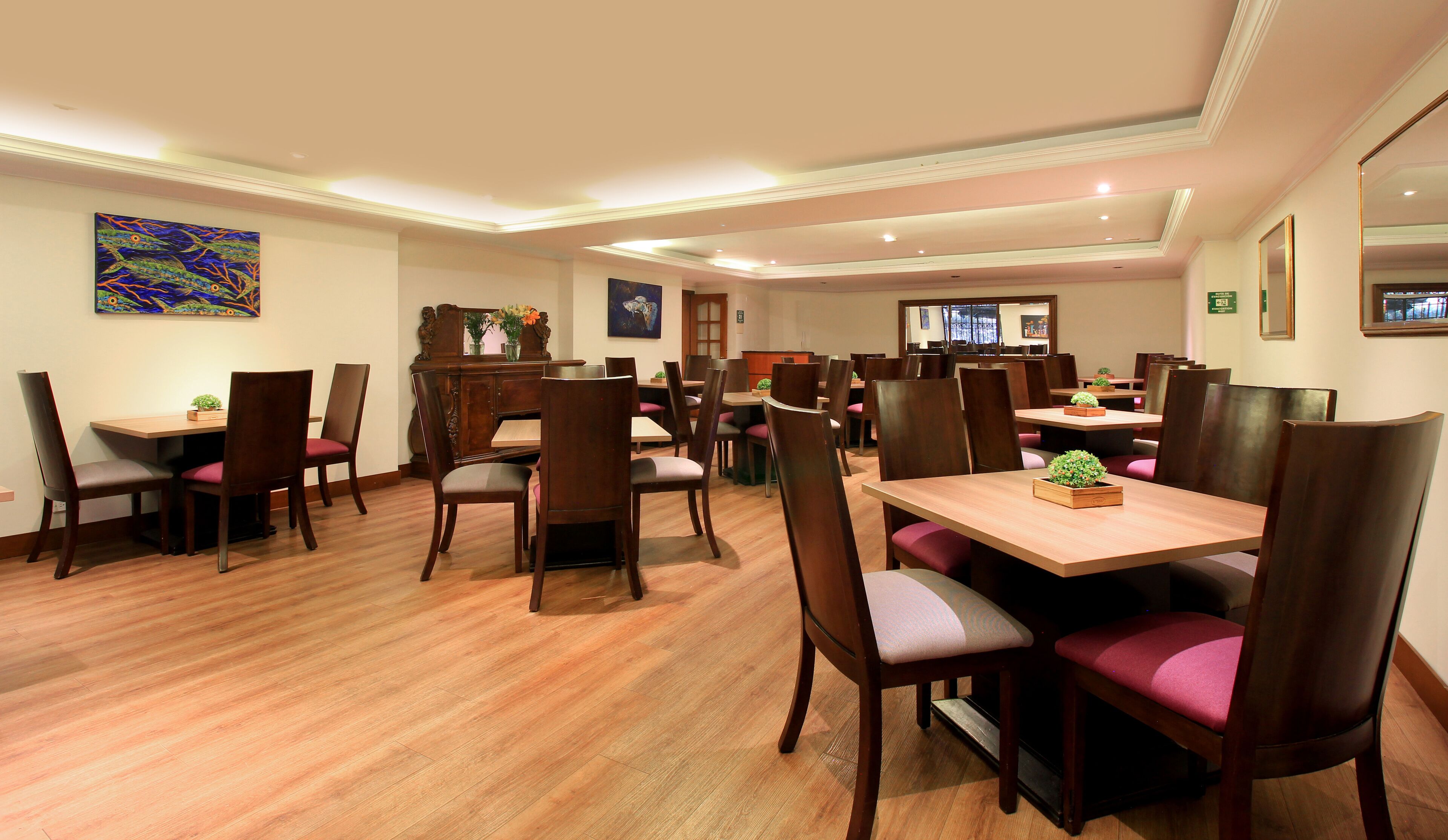 A spacious dining area with wooden tables and chairs, a large mirror, and artwork on the walls.