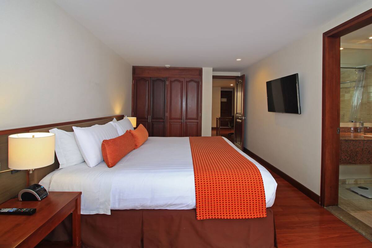 A hotel room with a large bed, a TV mounted on the wall, and a wooden wardrobe.
