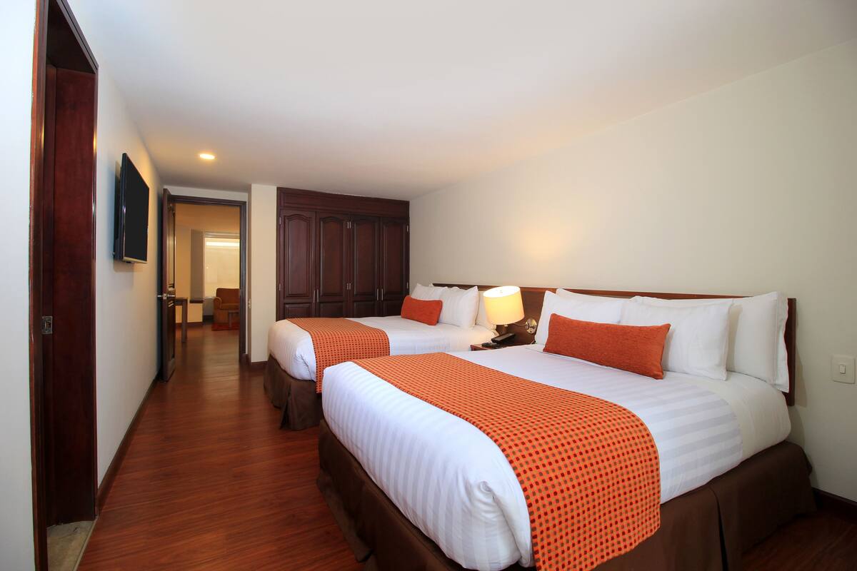 A hotel room with two beds, wooden flooring, a wardrobe, and a television.