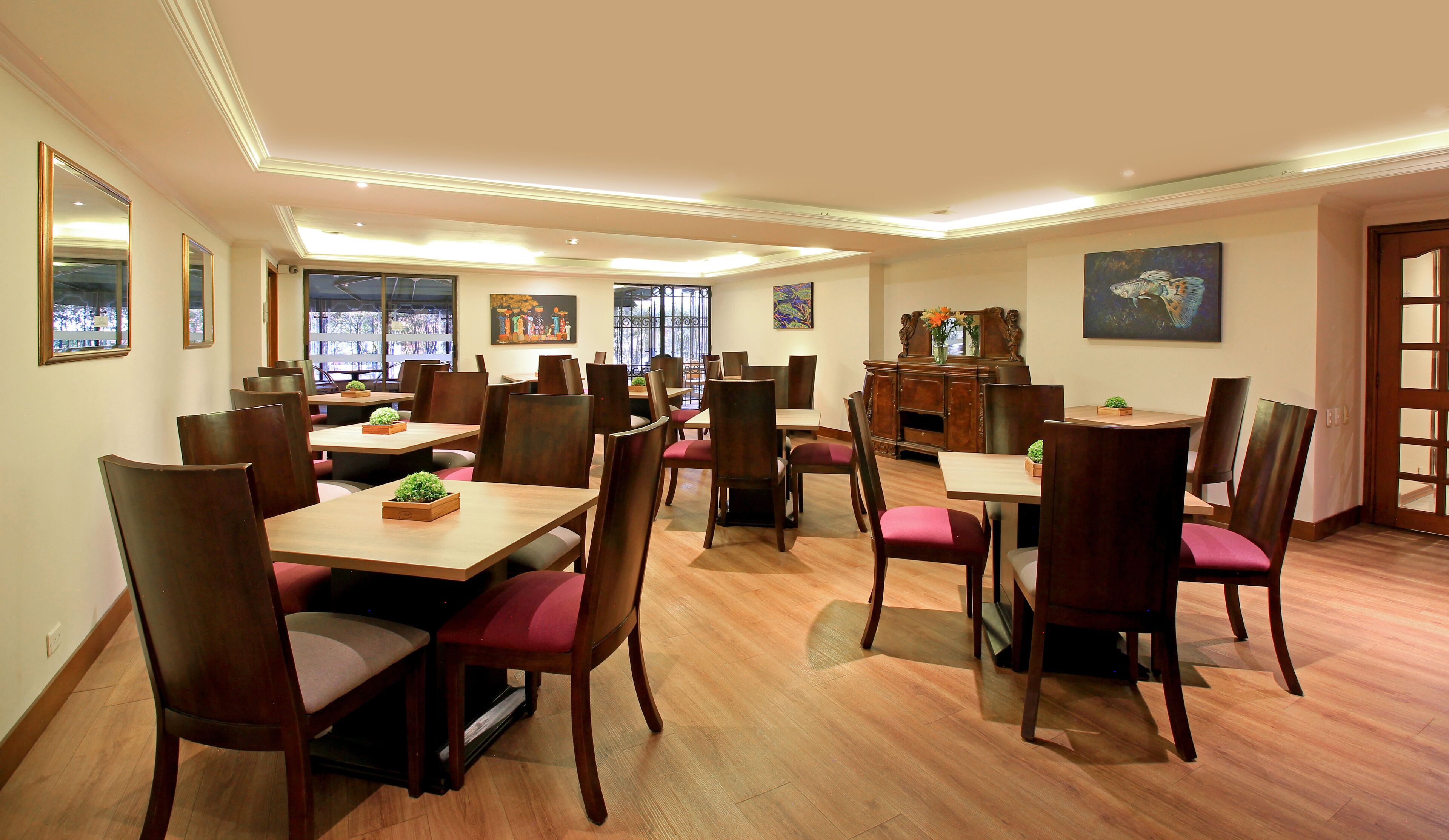 A dining area with wooden tables and chairs, a central decorative cabinet, and artwork on the walls.
