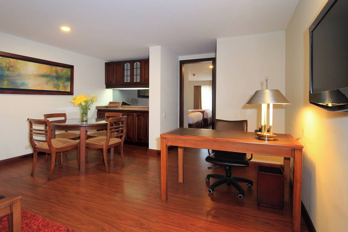 A hotel room with a dining area, kitchenette, and a TV mounted on the wall.