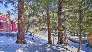 Bosque cubierto de nieve con un edificio rojo, un conjunto de columpios y un letrero que indica una estación de servicio forestal.
