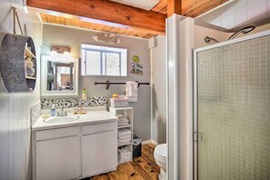 Ein Badezimmer mit Holzboden, einem Waschbecken mit Spiegel, einem Fenster und einer Duschkabine.