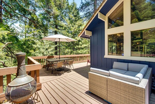 A wooden deck with outdoor furniture, a large window, and a view of trees. - Twin Peaks Cabin < 4 Mi to Lake Arrowhead! (Twin Peaks)