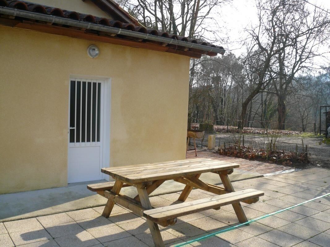Une table de pique-nique en bois se trouve à l’extérieur d’un bâtiment doté d’un patio carrelé.