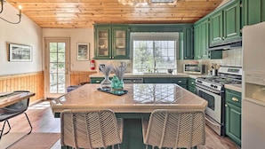 A kitchen with wooden ceiling, green cabinets, a central island with chairs, and a stove. - Calming Twin Peaks Family Retreat w/ Views! (Twin Peaks)