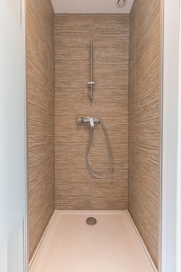 A shower with a vertical handle and a handheld showerhead in a corner with wooden walls.
