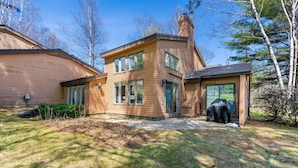 A two-story house with a chimney, a covered grill, and a stone wall. - Sauna Condo with Golf Views, Coach Road (Quechee)