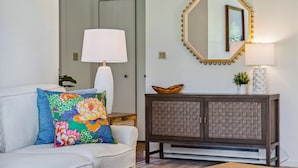 A living room with a white sofa, colorful pillows, a woven cabinet, and a mirror with lights. - Sauna Condo with Golf Views, Coach Road (Quechee)