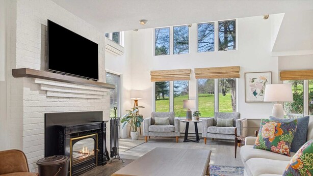 A spacious living room with a fireplace, a television, and a large window overlooking a garden. - Sauna Condo with Golf Views, Coach Road (Quechee)