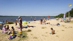 Een strand met mensen die zonnebaden en zwemmen, een vlag en een heldere lucht.