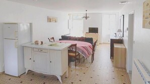 Een compacte keuken met een koelkast, een eethoek met tafel en stoelen, en een slaapkamer met een bed en een televisie.