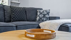 Moderni olohuone, jossa on harmaa sohva, kuviollisia koristetyynyjä, valkoinen huopa ja punottu kori puupöydällä.