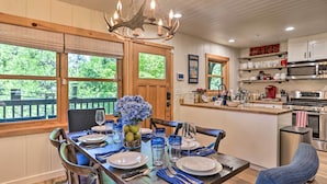 Un coin repas avec une table en bois dressée pour quatre personnes, un lustre et une vue sur l’extérieur.