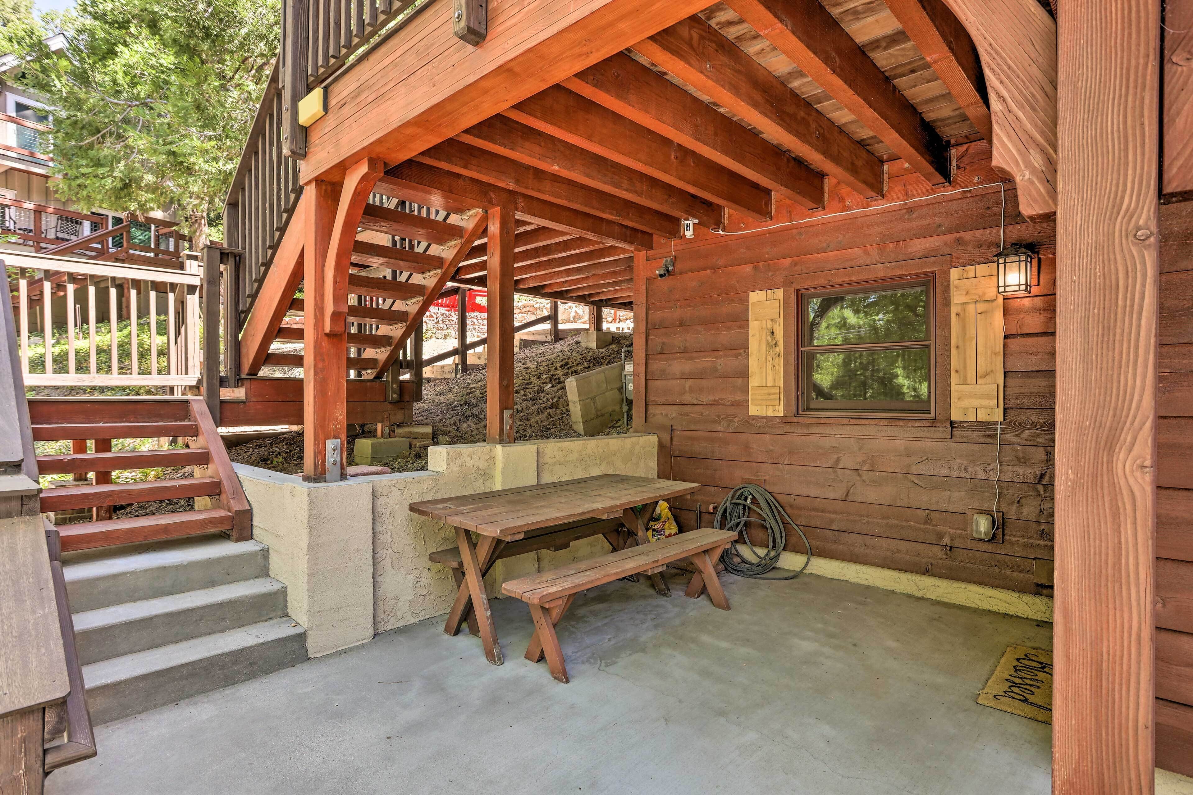 Una cabaña de madera con mesa de picnic, banco, escalera y ventana con vista a los árboles.