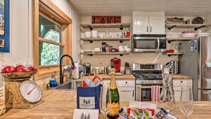 A kitchen with wooden shelves, a scale, a bottle of champagne, and a bowl of snacks. - Steps to Lake: Cabin w/ Deck in Lake Arrowhead (Cedar Glen)
