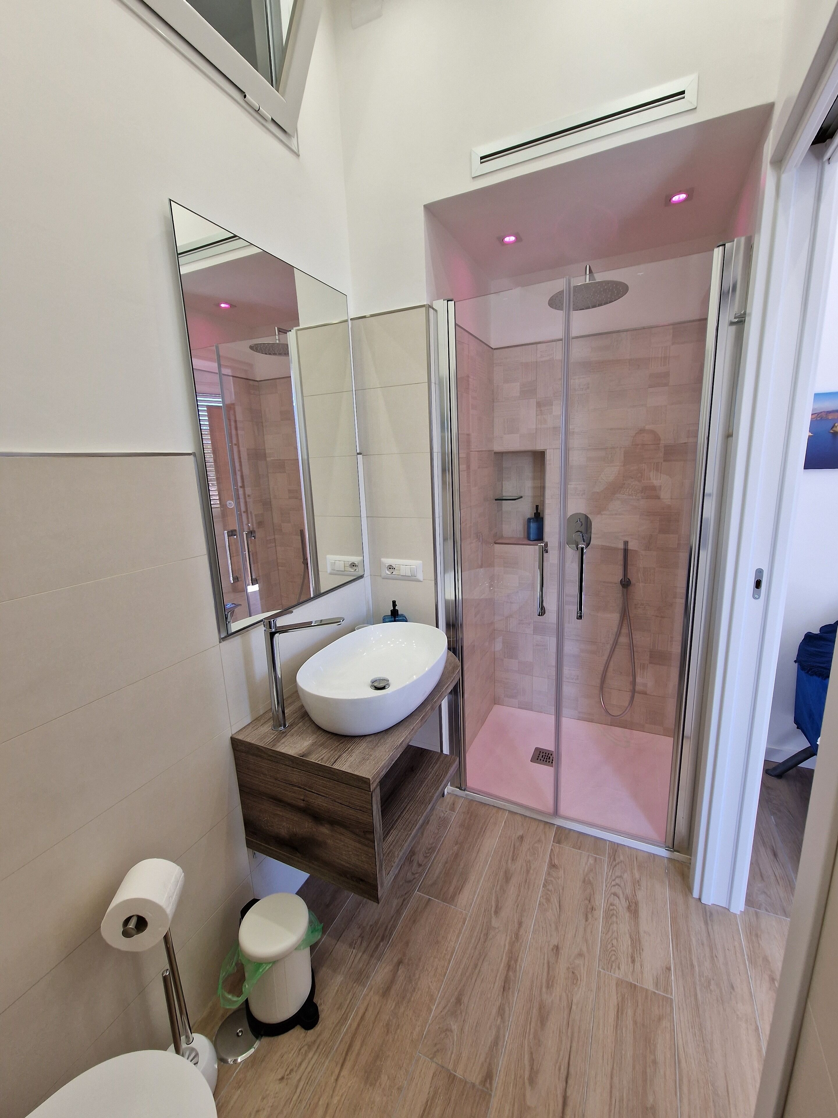 A modern bathroom with a glass-enclosed shower, a white sink, and a wooden vanity.