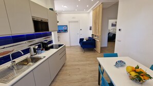 A modern kitchen with a built-in stove, a sink, and a dining area with a table and chairs. - New apartment 100 meters from the sea (Nerano)