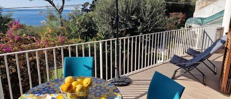 En balkon med et bord, stole og udsigt til stranden.