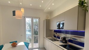 A modern kitchen with a white countertop, blue backsplash, and a dining area with a table and chairs. - New apartment 100 meters from the sea (Nerano)