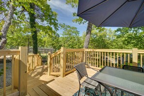 Un patio in legno con tavolo e sedie in vetro, immerso tra gli alberi.
