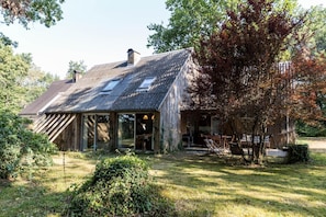 Une maison rustique en bois, dotée d’un toit en pente, de grandes fenêtres et d’un patio aménagé avec des meubles d’extérieur.
