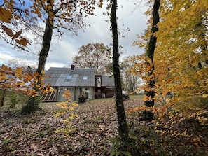 A rustic house surrounded by trees with autumn leaves, a clear sky, and a well-maintained lawn.