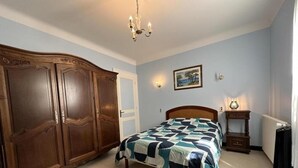 A bedroom with a bed, a wardrobe, a nightstand, and a wall-mounted lamp. - Les tilleuls - SOUSTONS (SOUSTONS)