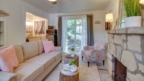Una sala de estar con un sofá color crema, un sillón estampado, una chimenea de piedra y vistas al exterior a través de ventanas amplias.