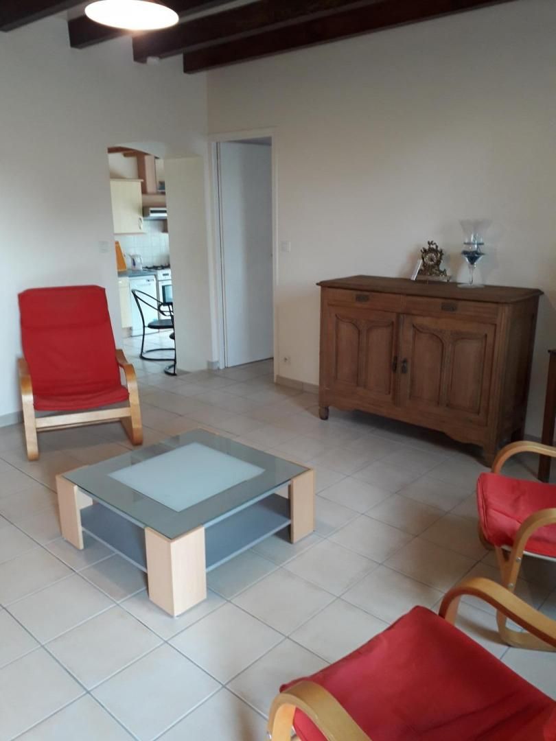 A living room with a glass-top coffee table, red upholstered chairs, a wooden cabinet, and a doorway leading to another room.
