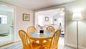Un coin repas avec une table ronde en bois et six chaises, un petit objet noir posé sur la table, et une lampe sur pied à droite.