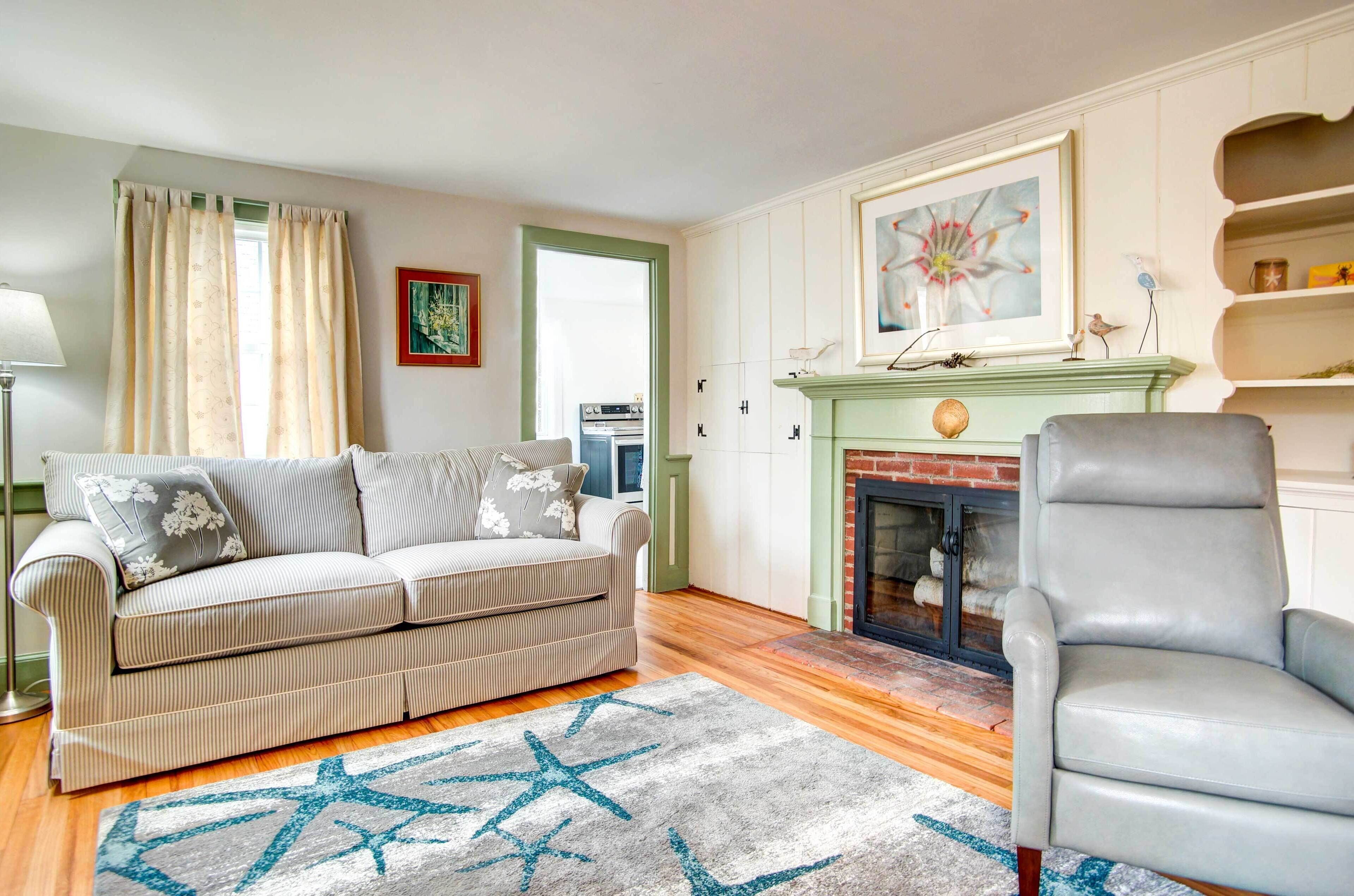 A living room with a sofa, armchair, fireplace, and artwork.