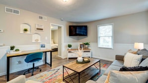 Un salon moderne comprenant un canapé, une table basse, un téléviseur et un bureau avec une chaise.
