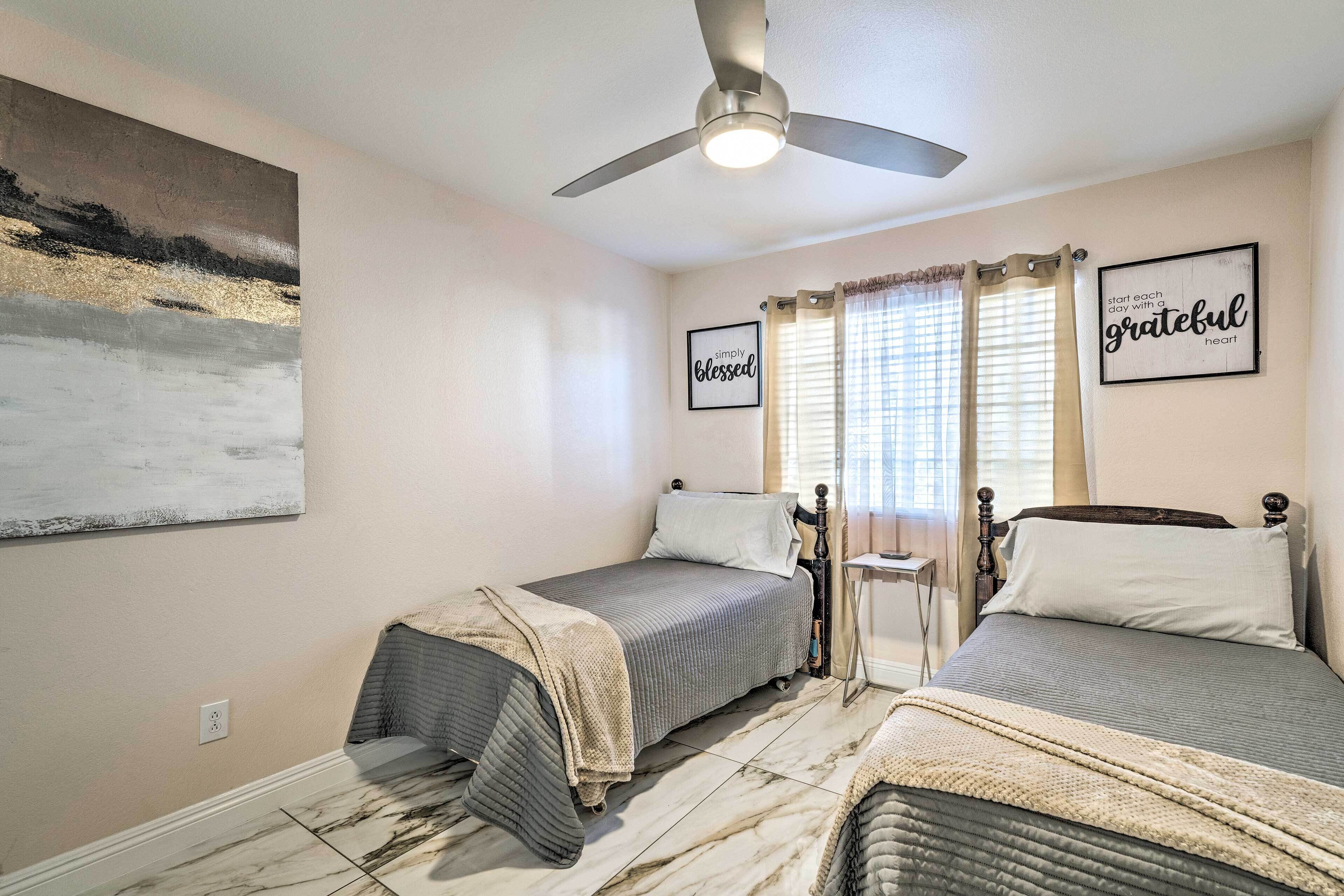 A bedroom with two beds, a ceiling fan, and a painting on the wall.