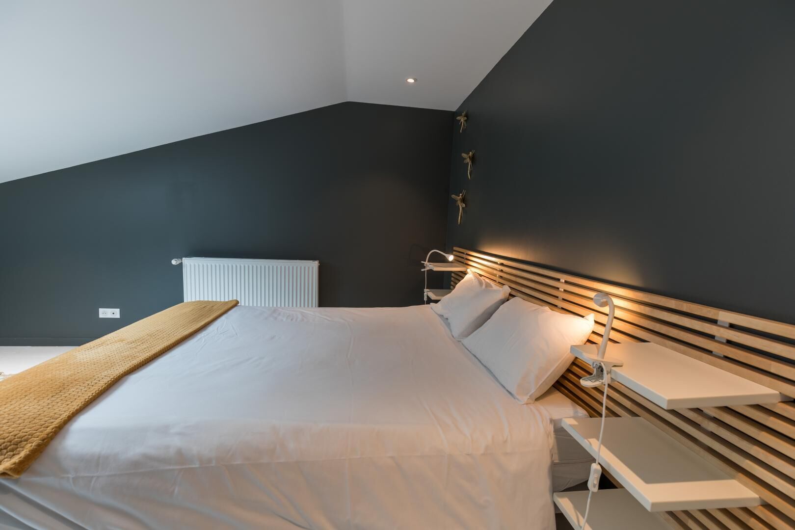 Una camera da letto moderna con un letto grande, comodini, termosifone e soffitto spiovente.
