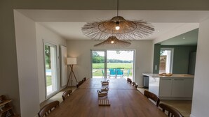 A spacious dining area with a long wooden table, wicker baskets, and a unique woven light fixture. - Villa Cassora - Herm (HERM)