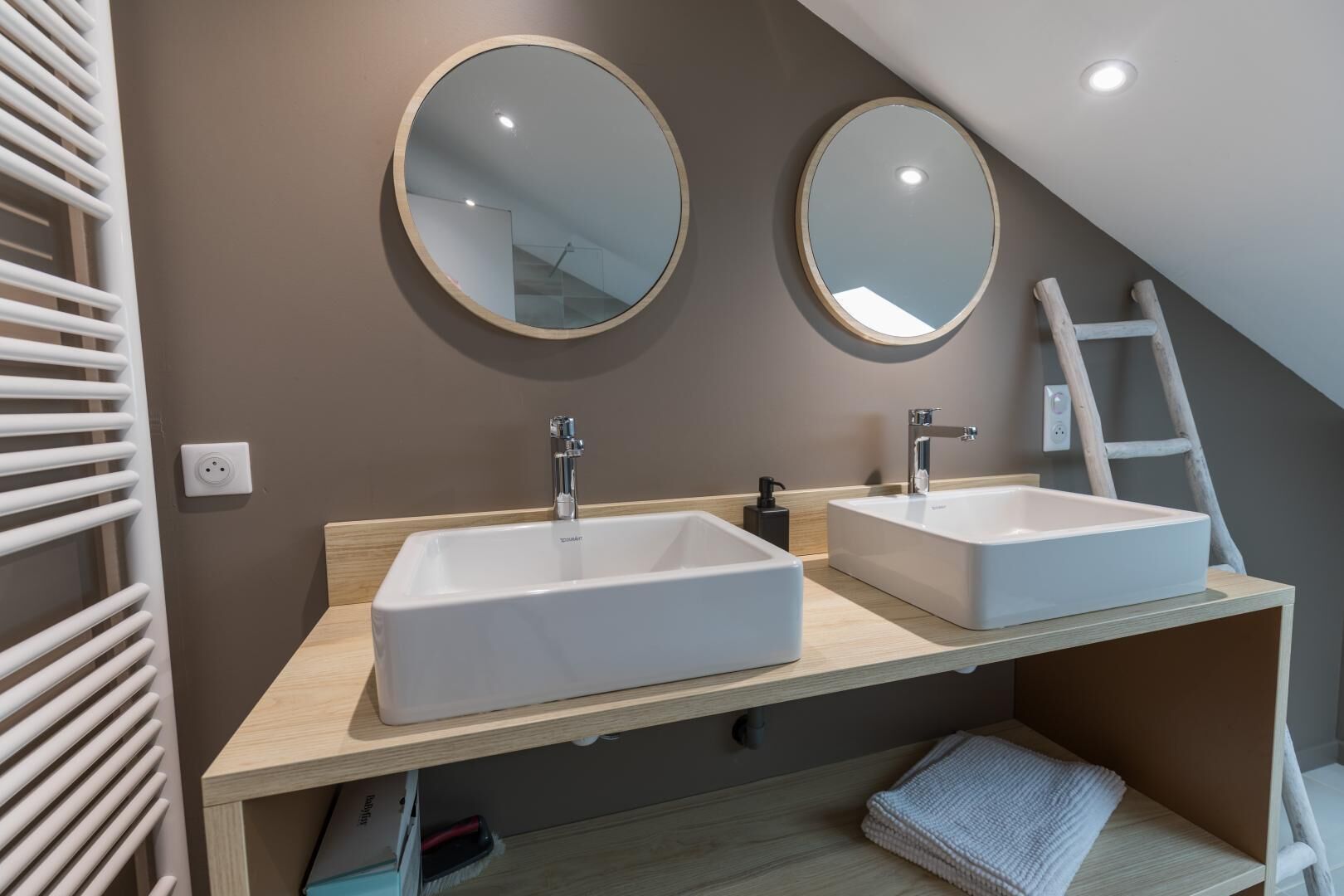 A modern bathroom with two sinks, a wooden vanity, and two round mirrors.