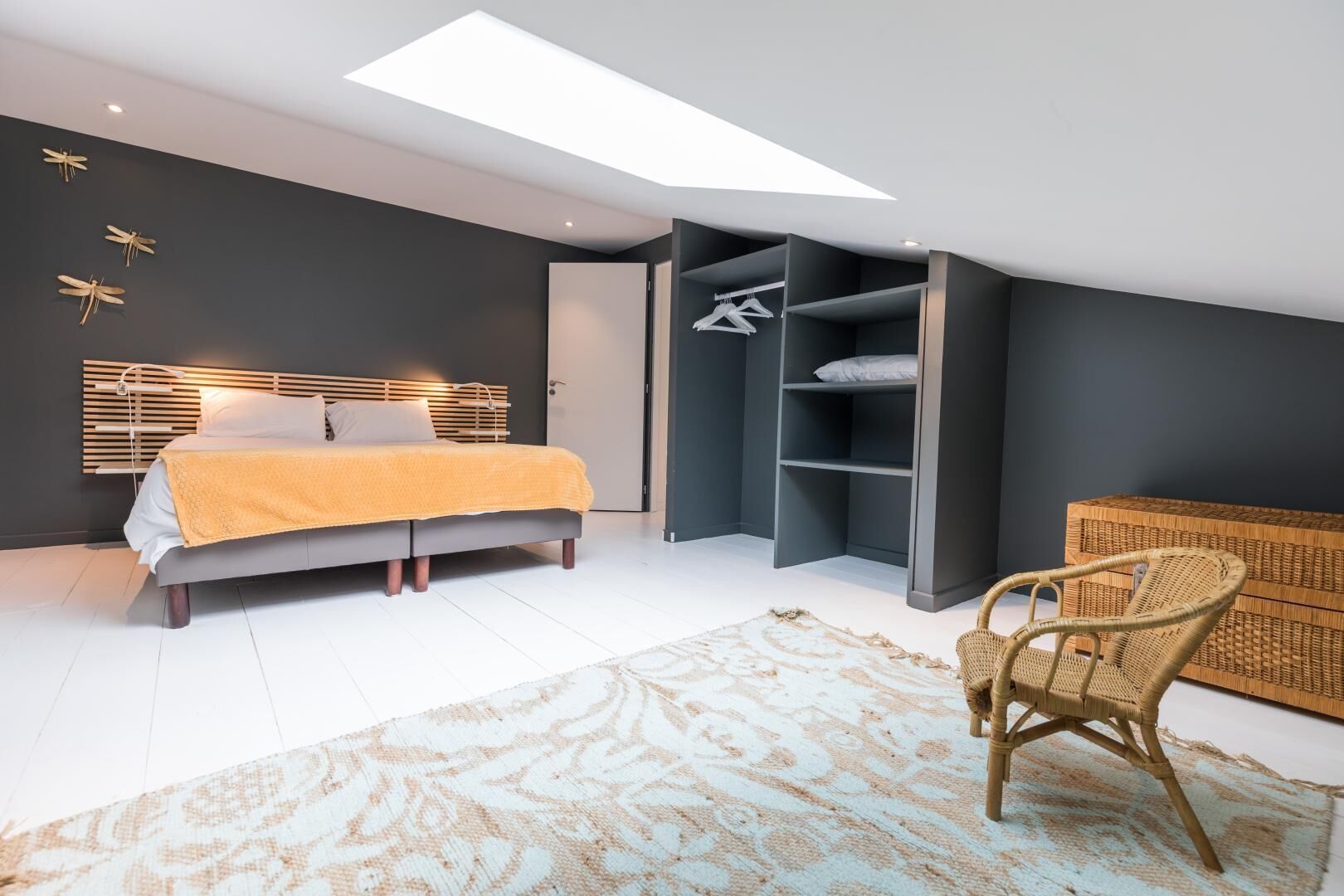 A modern bedroom with a bed, a built-in wardrobe, a wicker chair, and a skylight.