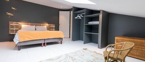 A modern bedroom with a bed, a built-in wardrobe, a wicker chair, and a skylight.