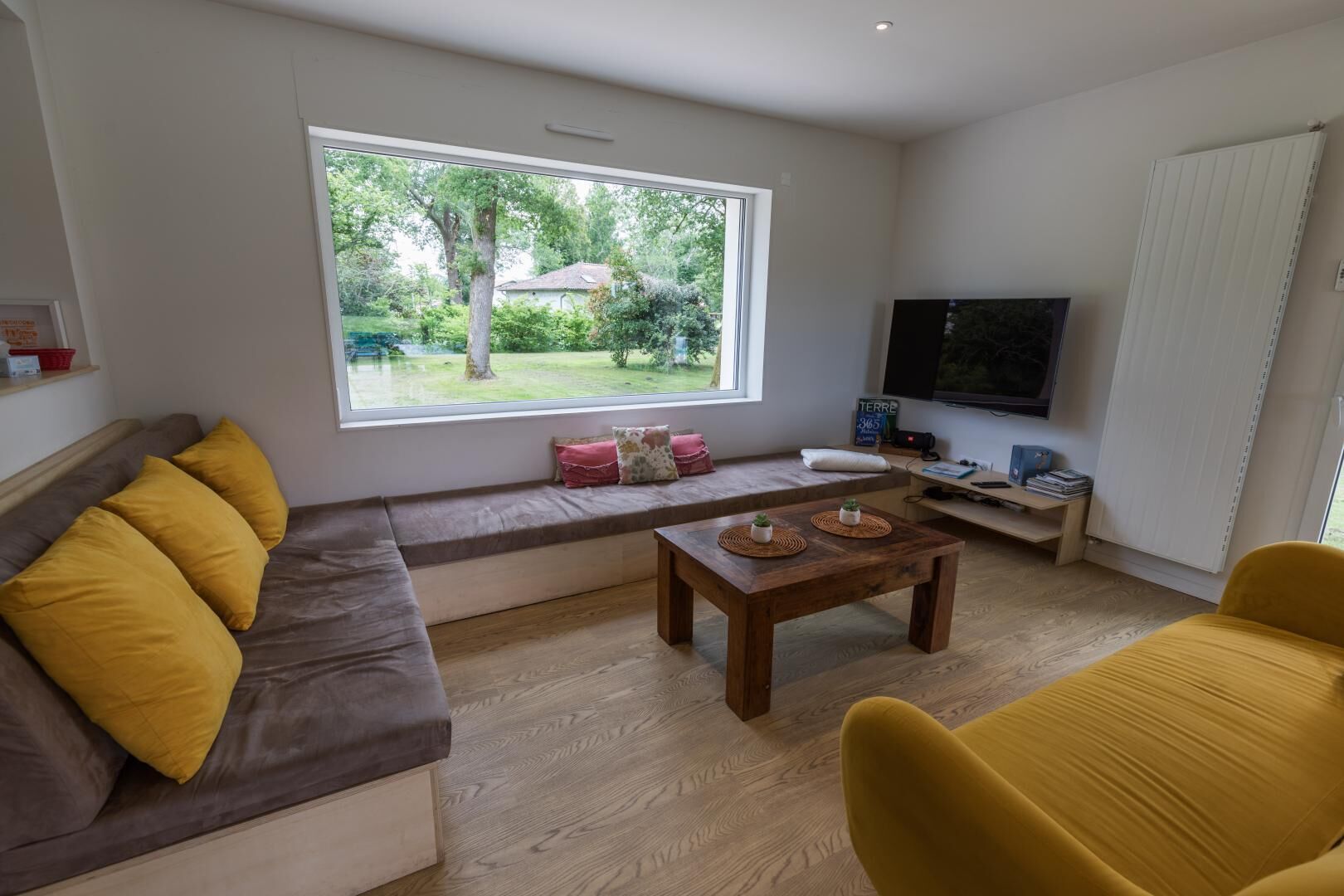 A modern living room with a large window, a sofa with cushions, a coffee table, and a television.