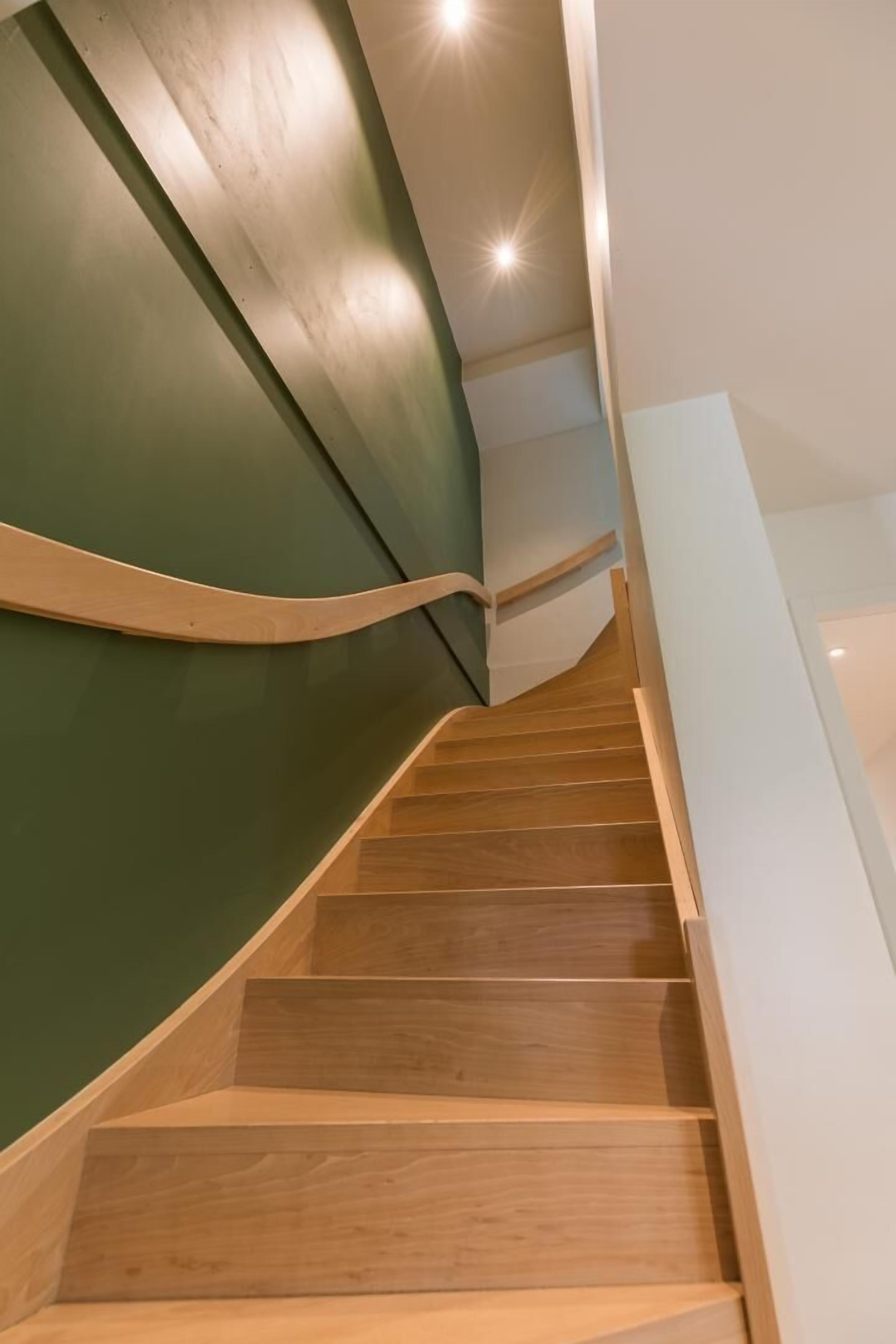 A wooden staircase with a green wall on one side and a white wall on the other.