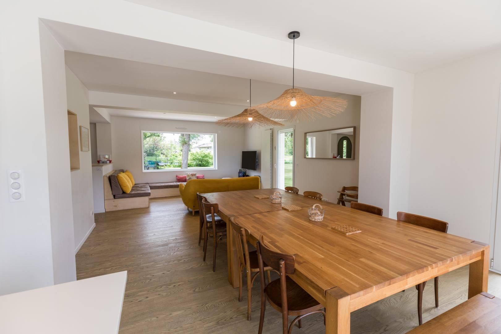 Un comedor amplio con una mesa y sillas de madera, un sofá amarillo y un ventanal que proporciona luz natural.