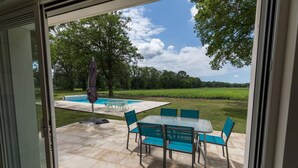 A patio area with a pool, outdoor furniture, and a view of a green landscape. - Villa Cassora - Herm (HERM)